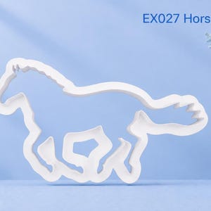 May include: A white plastic cookie cutter in the shape of a galloping horse. The product is labelled with the text EX027 Horse Galloping. The design features a continuous outline of the animal in motion, showing the head, legs, and tail.
