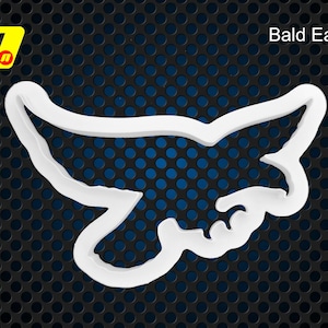 May include: White plastic cookie cutter shaped like a bald eagle. The cutter is on a black and blue background.
