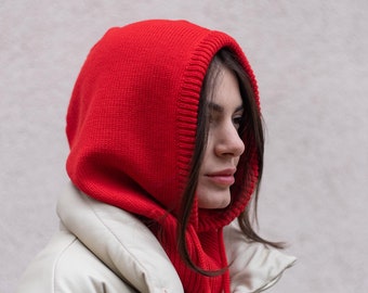 May include: A woman wearing a red knitted hooded scarf over a white puffer jacket.