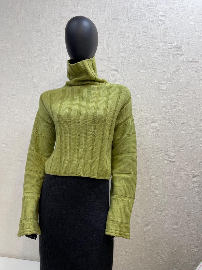 May include: A lime green ribbed knit turtleneck sweater with long sleeves. The sweater is paired with a dark gray pencil skirt. The outfit is displayed on a mannequin with a black head.