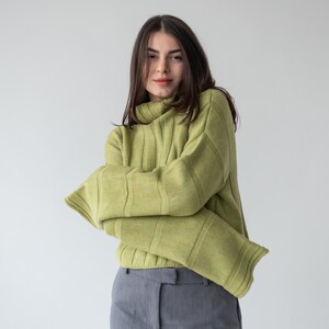 May include: A light green ribbed knit sweater with a turtleneck and long sleeves. The sweater is paired with gray trousers. The outfit is simple and stylish, suitable for casual wear.
