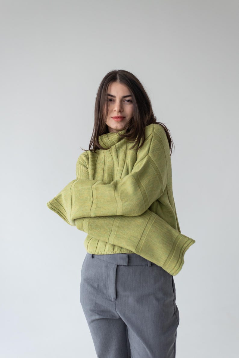 May include: A light green ribbed knit sweater with a turtleneck and long sleeves. The sweater is paired with gray trousers. The outfit is simple and stylish, suitable for casual wear.