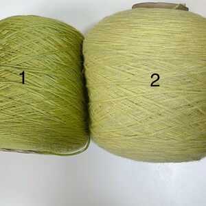 May include: Two spools of yarn in shades of green. One is a cone shape, labeled "1", and the other is a round shape, labeled "2". The yarn appears to be a natural fiber, suitable for knitting or crochet projects.