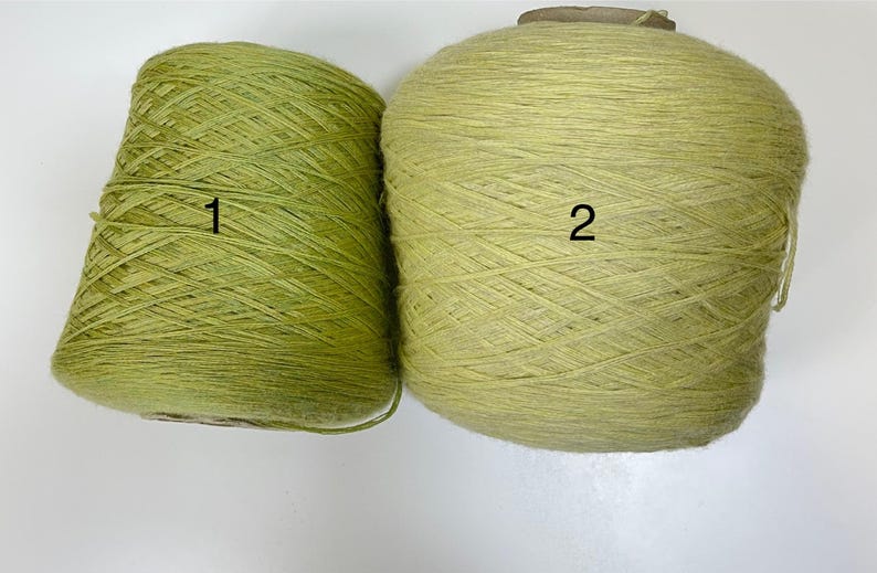 May include: Two spools of yarn in shades of green. One is a cone shape, labeled "1", and the other is a round shape, labeled "2". The yarn appears to be a natural fiber, suitable for knitting or crochet projects.