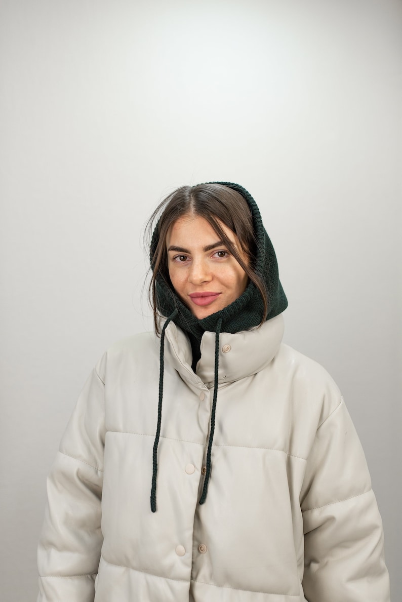 Puede incluir: Una mujer con una chaqueta acolchada blanca con un cuello de lana con capucha verde oscuro. La chaqueta tiene una cremallera y cierre de bot&oacute;n.
