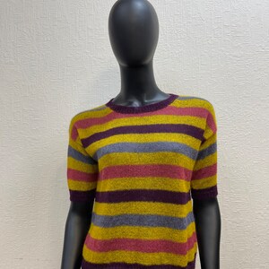 May include: A striped short-sleeved sweater in shades of yellow, purple, pink, and gray. The sweater is made of a soft, fuzzy material.