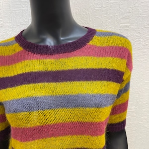 May include: A striped sweater with yellow, purple, pink, and gray stripes. The sweater has a crew neck and short sleeves.