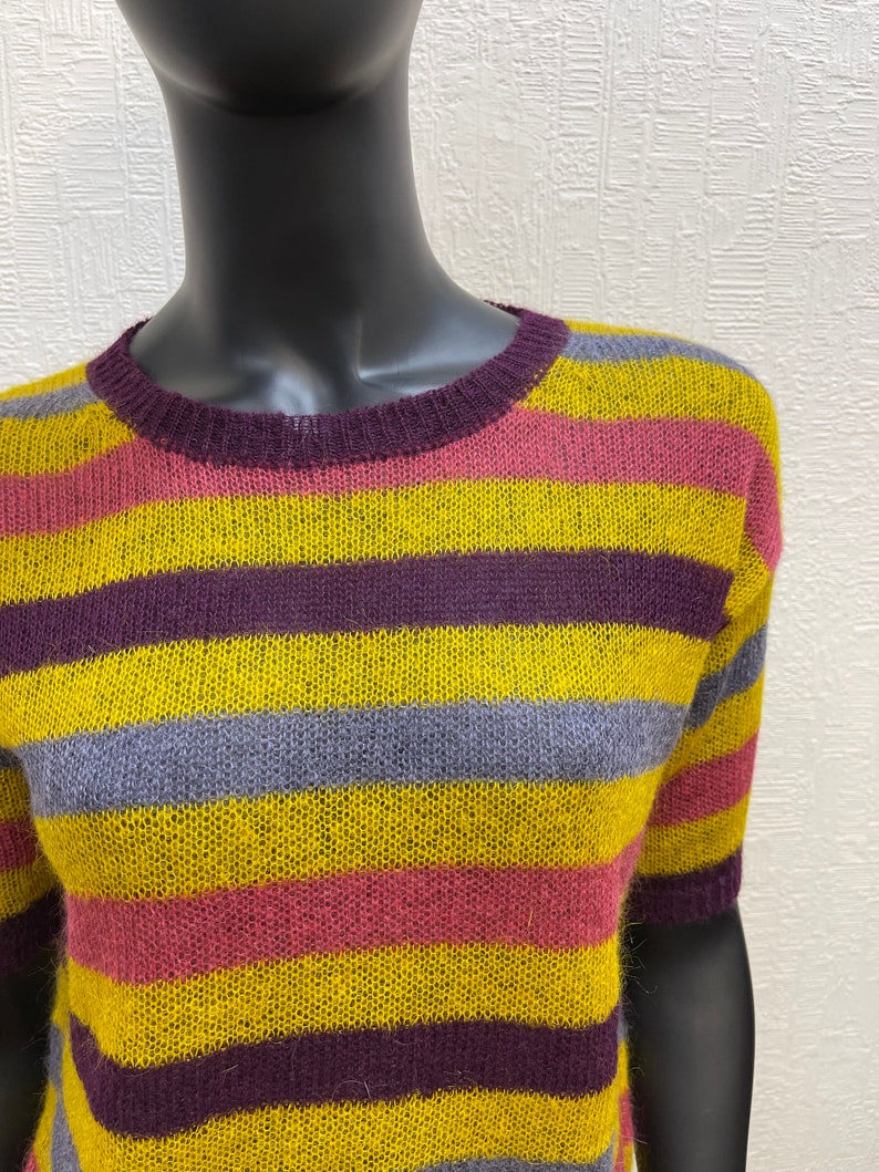 May include: A striped sweater with yellow, purple, pink, and gray stripes. The sweater has a crew neck and short sleeves.
