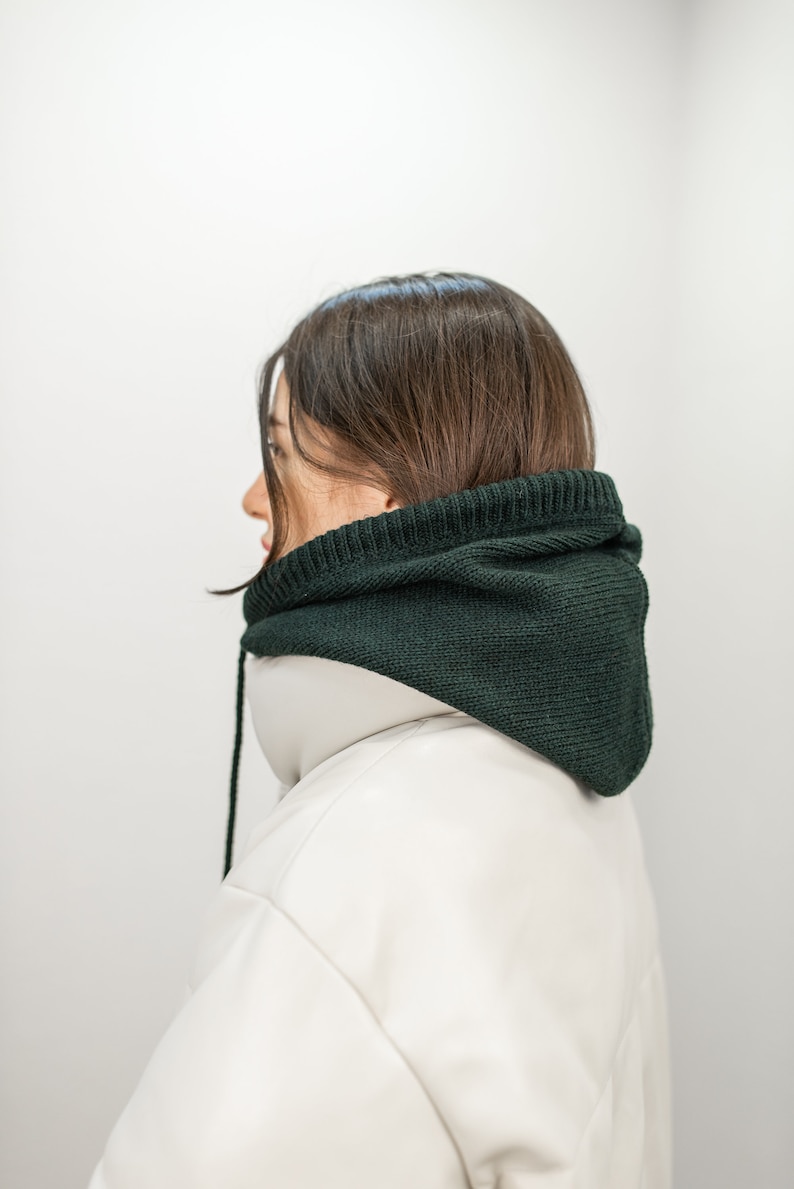 May include: A person wearing a white puffer jacket with a dark green knitted hood.