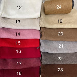 Puede incluir: Primer plano de una pila de muestras de tela en varios colores, incluyendo blanco, beige, rosa, rojo, burdeos, gris, marr&oacute;n y tostado. Las muestras est&aacute;n numeradas del 12 al 24.