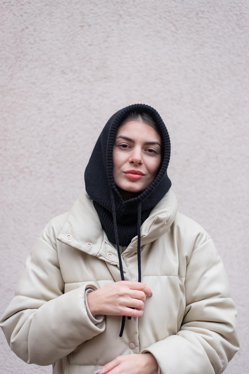 Puede incluir: Una mujer con un cuello de lana negro con capucha y una chaqueta acolchada blanca. El cuello tiene un cord&oacute;n.