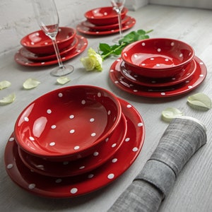 Op de afbeelding: Een set rood servies met witte stippen. De set bevat een groot dinerbord, een kleiner saladebord en een soepkom. De borden en de kom zijn allemaal rood met witte stippen.