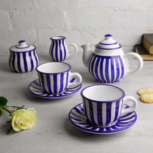 Op de afbeelding: Een blauw en wit gestreept theeservies met een theepot, roomkan, suikerpot en twee kopjes en schoteltjes.