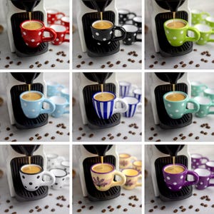 May include: Nine espresso cups with different polka dot patterns. The cups are white with black, red, blue, green, purple, and yellow polka dots. The cups are arranged in a grid pattern with a coffee machine in the background.