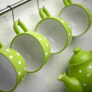 May include: A set of four green teacups with white polka dots hanging on a rack, along with a matching green teapot with white polka dots.