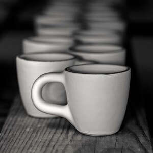 May include: A set of white ceramic coffee mugs with a subtle rim detail. The mugs are arranged in a row, with the closest mug in focus.