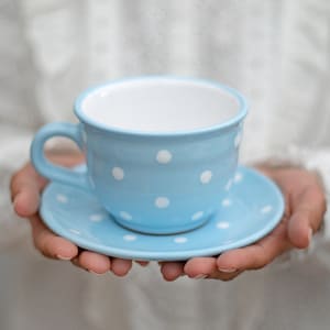 May include: A light blue teacup and saucer with white polka dots. The teacup has a rounded handle and the saucer is slightly larger than the teacup.