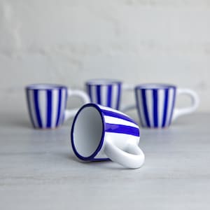 May include: Four white ceramic mugs with blue stripes. One mug is lying on its side, while the other three are standing upright.