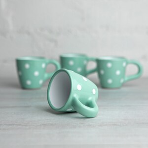 May include: Four mint green ceramic mugs with white polka dots. One mug is lying on its side, while the other three are standing upright.