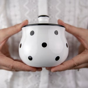 May include: A white ceramic sugar bowl with a black lid and black polka dots.