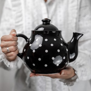 May include: A black ceramic teapot with white polka dots. The teapot has a rounded body and a spout on the side.