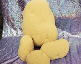 May include: Four plush potato shaped pillows in various sizes. The largest potato is in the back, with two smaller potatoes in front of it, and a smaller potato in front of those.