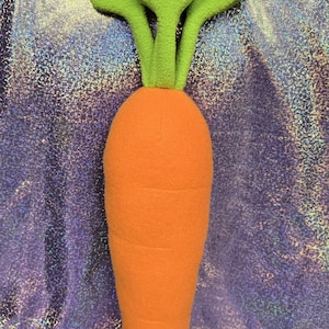 Puede incluir: Un juguete de peluche en forma de zanahoria con hojas de fieltro verde. La zanahoria es naranja y tiene una superficie texturizada.