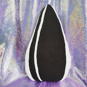 May include: A black and white plush pillow shaped like a sunflower seed. The pillow is made of soft, fuzzy fabric and has a white outline around the black center.