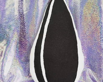 Può includere: Un cuscino di peluche nero e bianco a forma di seme di girasole. Il cuscino è realizzato in tessuto morbido e soffice e ha un contorno bianco attorno al centro nero.