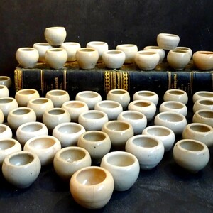 May include: A collection of over 40 small, white ceramic bowls arranged in a pyramid shape. The bowls are all approximately the same size and shape, and they have a slightly textured surface.