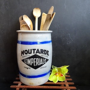 Puede incluir: Un tarro de cerámica blanco con rayas azules y una etiqueta negra que dice "MOUTARDE GARANTIE L'IMPERIALE MARQUE DEPOSEE" contiene cucharas de madera.