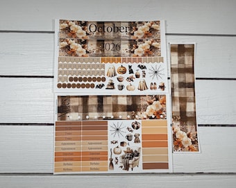 May include: A set of October 2026 calendar planner stickers featuring a brown plaid pattern, floral accents, and Halloween-themed illustrations including ghosts, pumpkins, cats, and spiderwebs. The sheet includes date markers, to-do lists, and labels.