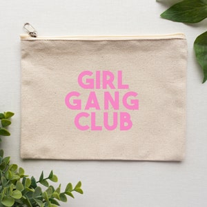 Può includere: Una pochette con cerniera in tela naturale con una grafica rosa che recita "GIRL GANG CLUB".