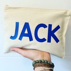 May include: A white canvas zippered pouch with the name "JACK" printed in bold blue letters.