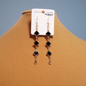 May include: A pair of gold earrings with black square-shaped stones hanging from a chain. The earrings are on a white card with the text "Fashion Jewelry 4885".