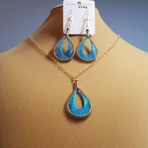 May include: A turquoise blue and gold necklace and earrings set with a teardrop pendant and matching earrings. The jewelry is displayed on a mannequin.