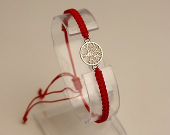 May include: Red string bracelet with a silver tree of life charm.