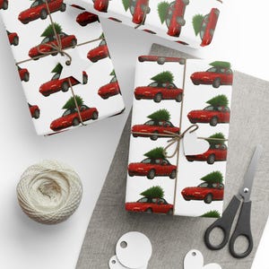 May include: White wrapping paper with a repeating pattern of red cars with Christmas trees on top. The wrapped gifts are tied with twine and have blank tags. A ball of twine, scissors, and blank tags are also visible.