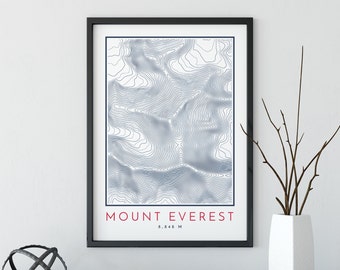 May include: A black framed print with a topographic map of Mount Everest. The map is in shades of blue and white. The text "MOUNT EVEREST 8,848 M" is printed in red at the bottom of the print.