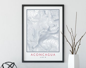 May include: A black framed print with a topographic map of Aconcagua, the highest mountain in the Andes, in blue lines on a white background. The text "ACONCAGUA 6,961 M" is printed in red at the bottom of the print.