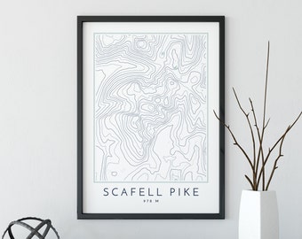 May include: A black framed print with a topographic map of Scafell Pike, a mountain in England. The print includes the name "Scafell Pike" and the elevation "978 M".