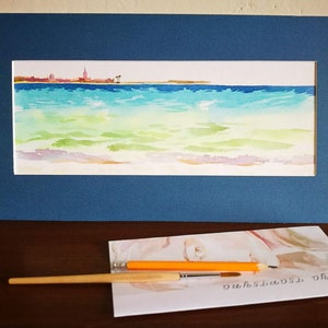 May include: A framed watercolor painting of a seascape with a city skyline in the distance. The water is a light blue and green, with whitecaps and ripples. The sky is a pale blue.