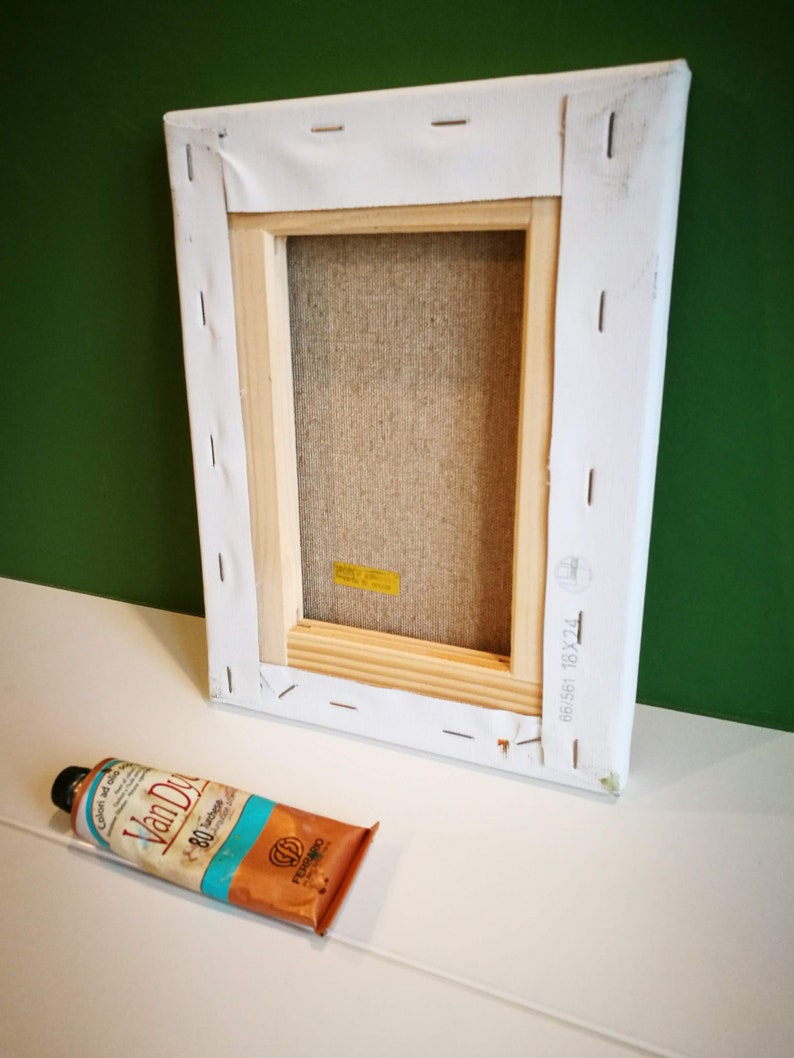 May include: A white canvas stretched over a wooden frame with the text "681581 18X24" printed on the side. A tube of Van Dyke brown oil paint is lying on a white surface.