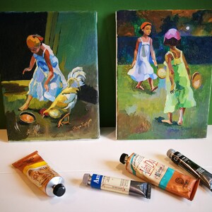 Puede incluir: Dos pinturas enmarcadas sobre una superficie blanca. La pintura de la izquierda muestra a una joven con un vestido azul alimentando a un gallo desde un cuenco. La pintura de la derecha muestra a dos j&oacute;venes con vestidos caminando por un campo por la noche. Hay tres tubos de pintura en la superficie.