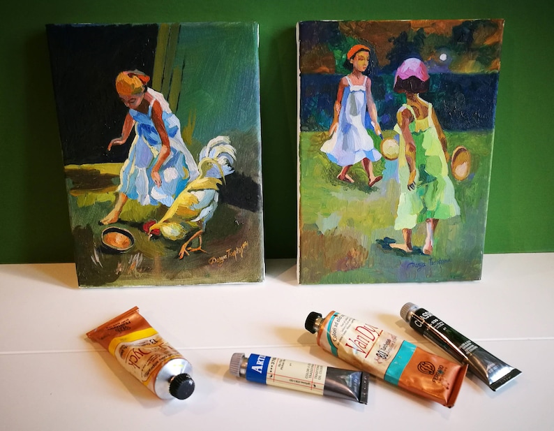 Puede incluir: Dos pinturas enmarcadas sobre una superficie blanca. La pintura de la izquierda muestra a una joven con un vestido azul alimentando a un gallo desde un cuenco. La pintura de la derecha muestra a dos j&oacute;venes con vestidos caminando por un campo por la noche. Hay tres tubos de pintura en la superficie.