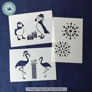 May include: White stencils with bird and snowflake designs. Includes puffins with gifts and flamingos with a present. The stencils are on a dark blue background. Text on the image reads "Image Copyright Stencil Stash".