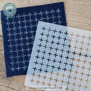 Può includere: Uno stencil di plastica bianca con un motivo ripetitivo di segni più. Lo stencil è posizionato sopra un tessuto di jeans blu con lo stesso motivo di segni più, ma in un colore più chiaro. Il testo "Image Copyright Stencil Stash" è stampato nella parte inferiore dello stencil.