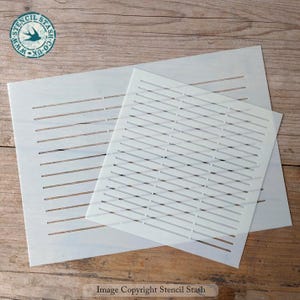May include: Two white stencils with horizontal and diagonal line patterns. The stencils are made of a translucent material and are placed on a wooden surface. The image includes the text "Stencil Stash" and a logo.