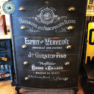 Może przedstawiać: Czarna komoda w stylu vintage z pięcioma szufladami. Każda szuflada jest oznaczona białym tekstem w języku francuskim, w tym "Parfumerie aux Principes des Fleurs" i "Esprit de Verveine". Komoda ma uchwyty w kolorze mosiądzu.