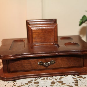 Puede incluir: Una bandeja de valet de madera con un cajón y varios compartimentos. La bandeja es marrón y tiene un diseño decorativo alrededor de los bordes.